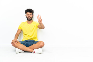 Young Moroccan handsome man sitting on the floor over isolated background happy and counting three with fingers