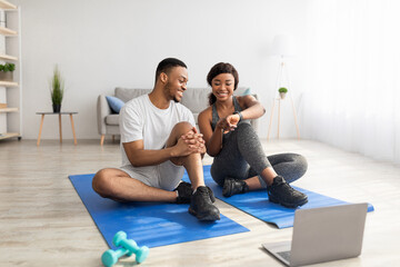 Young black couple taking break from home training, watching video sports tutorial on laptop pc,...