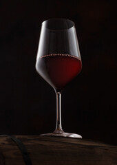 Crystal glass of red wine on top of wooden barrel on black.