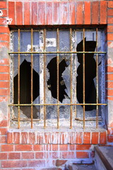 Zerbrochenes Glas eines vergitterten Fensters in einer Backsteinfassade
