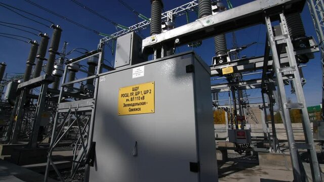 Oil circuit breaker cabinet with yellow information sign at electricity production substation under blue sky close view