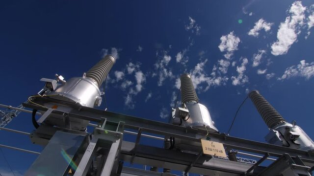 Motion past bushings with ceramic insulators on circuit breakers at production substation under blue sky close low angle shot
