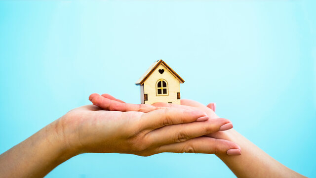 The hands of an adult and a child are holding a wooden house. Home for the family, insurance, safety, International Day of the Family, foster family
