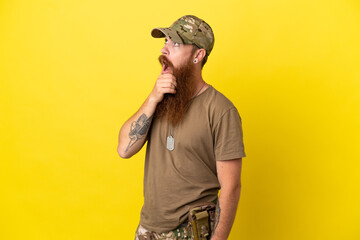 Redhead Military man with dog tag isolated on yellow background having doubts and with confuse face...