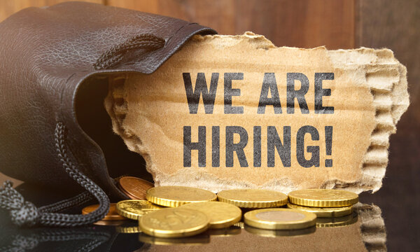 On the table is a bag of money from which sticks out cardboard with the inscription - WE ARE HIRING