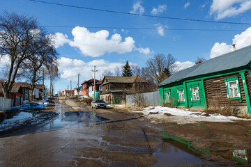 Scenic view of street in a small provincial town or village with traditional Russian wooden houses under blue sky. Spring rural landscape.  Nerekhta, Kostroma region, Russia