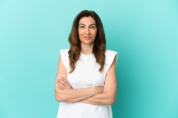 Middle aged caucasian woman isolated on blue background keeping the arms crossed in frontal position