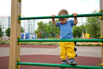 Fototapeta premium toddler boy climbs the sports ladder on the playground. sports lifestyle concept. walk in the fresh air. children play on the playground in summer.