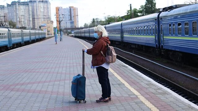 Adult blonde woman tourist in protective medical mask traveler standing with luggage at train station.