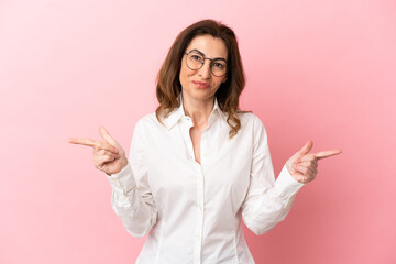 Middle aged caucasian woman isolated on pink background pointing finger to the laterals and happy