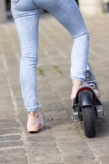 Close-up of female feet of a girl wearing pink sneakers and a jeans on electric kick scooter on the background of the city streets. High quality photo