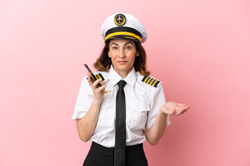 Airplane middle aged pilot woman isolated on pink background keeping a conversation with the mobile phone with someone