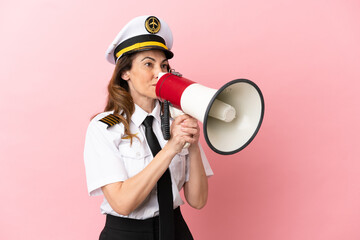 Airplane middle aged pilot woman isolated on pink background shouting through a megaphone