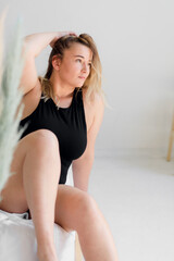 Naklejka premium body positive. A woman in black underwear poses on a modern white interior 