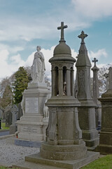 Fototapeta na wymiar Old historic grave monuments with crosses in Glasnevin, green cemetery with bare trees in , Dublin, Ireland.