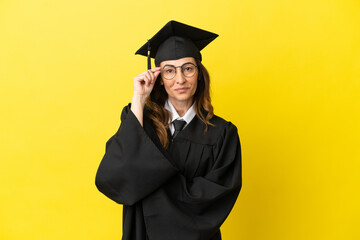 Middle aged university graduate isolated on yellow background with glasses and happy