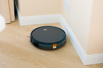 The circular robot vacuum cleaner collects debris from the living room floor. Black color.