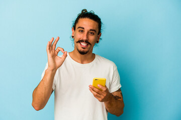 Young caucasian man with long hair holding mobile phone isolated on blue background cheerful and...