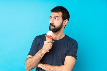 Young man with a cornet ice cream over isolated blue background with confuse face expression