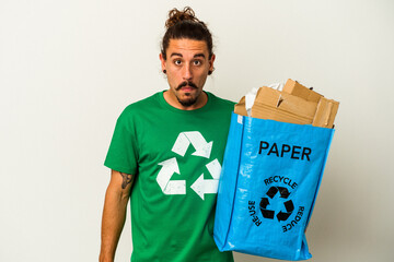Young caucasian man with long hair recycling cardboard isolated on white background shrugs...