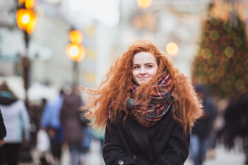 Red hair girl enjoying European Christmas Market. Blurred Lights on Christmas tree on background