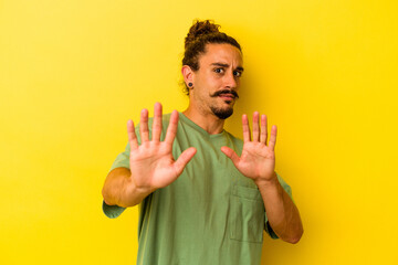Young caucasian man with long hair isolated on yellow background rejecting someone showing a...