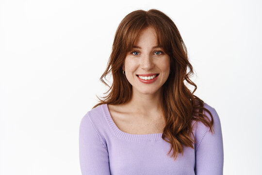Lifestyle and people concept. Smiling beautiful young woman in stylish clothes, with freckles and bangs, white teeth and natural face expression, standing against white background