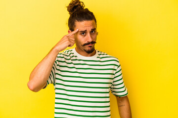 Young caucasian man with long hair isolated on yellow background pointing temple with finger, thinking, focused on a task.