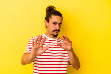Young caucasian man with long hair isolated on yellow background rejecting someone showing a...