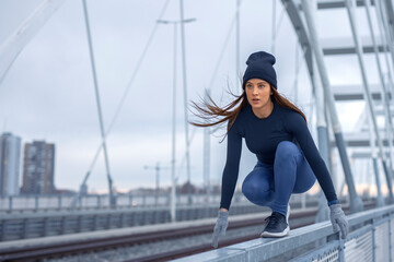 Young fitness woman in winter blue sportswear walks on bridge fence and practice body balance exercise during cold day