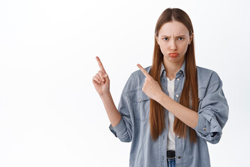 Sulking teenage girl pointing aside with jealous, unfair face, complaining looking displeased and...
