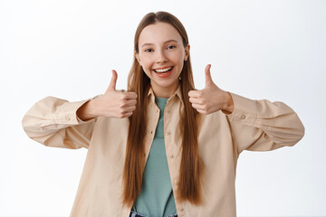 Supportive girl shows thumbs up, smiling and say yes, nod in approval, encourage you, praise for...