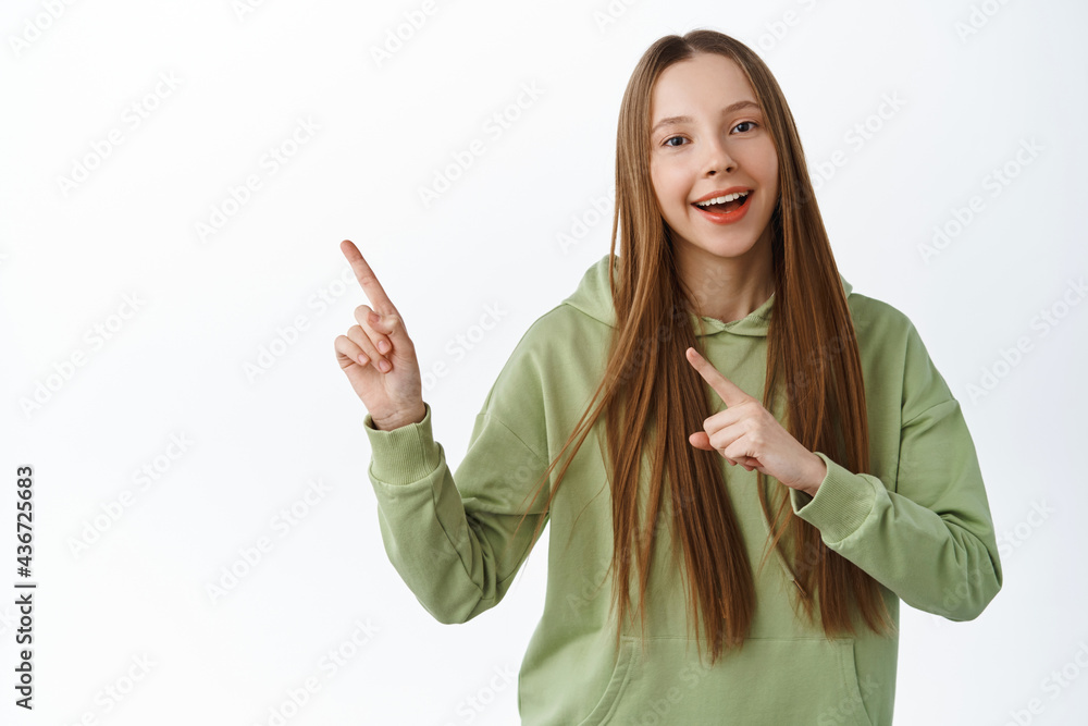 Wall mural looh this way. smiling teen girl demonstrate logo, pointing at banner, showing promo aside, standing