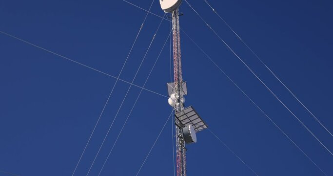 Tilting up shot of telecommunication towers, with a detailed look at its components like antennas, transmitters and wires, with clear sky above