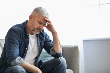 Upset senior man sitting on couch at home, copy space
