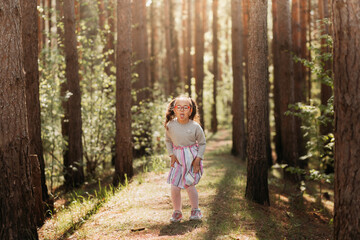 Cute girl with glasses makes a funny grimace and shows tongue in nature in summer