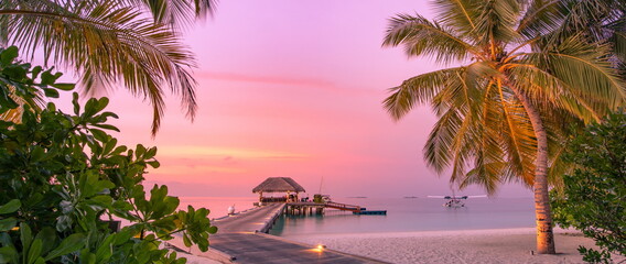 Amazing sunset panorama at Maldives. Luxury resort villas seascape, soft led lights under romantic colorful sky and palm tree leaves. Stunning travel beach landscape exotic relax vacation resort hotel