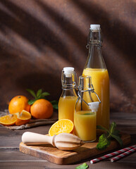 Fresh homemade orange juice in three bottles with citrus fruits on cutting board with morning shadows on a brown wooden background. Front view and copy space