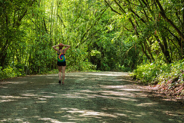 Woman with colorful backpack walking on rural road through tropical forest with copy space