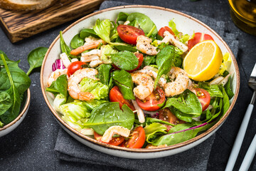 Shrimp salad with green leaves, tomatoes, octopus and ollive oil at black table.
