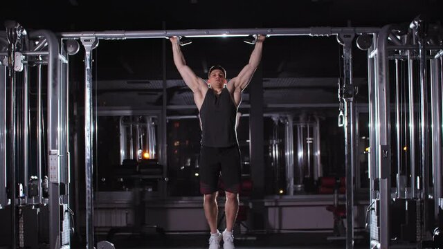 Handsome fit young man doing pull ups in the gym