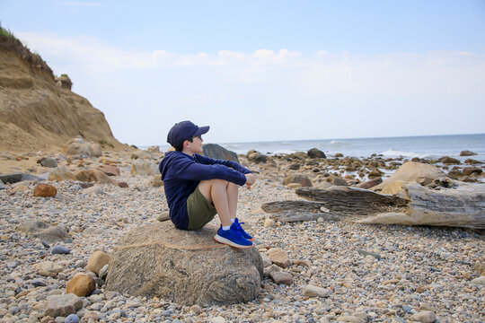 Boy sitting on a rock on the beach looking at the ocean