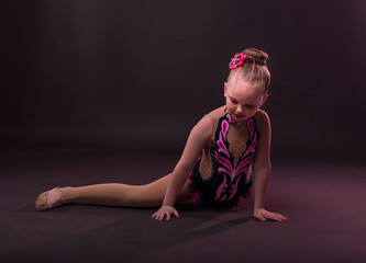 Funny cute little girl trying to do splits in gymnast costume, stretching.