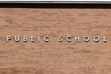 PUBLIC SCHOOL in stainless steel text against a brick background.