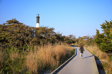 Child running on a boardwalk near a lighthouse at sunset