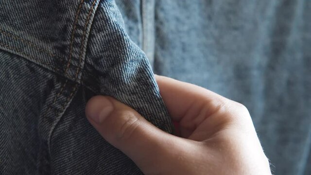Male hand touches blue denim jeans jacket, checking quality in the clothing store.