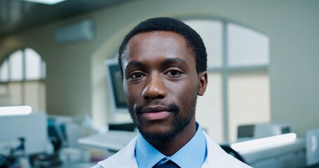 Obraz premium Close up portrait of happy positive African AMerican young man doctor in hospital looking at camera and smiling in good mood. Medicine, medical worker, young specialist in clinic, medic concept