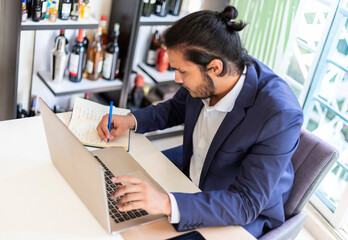 Young latino Businessman working at office. Laptop, pencil, stylus, watch, paper and male hands.