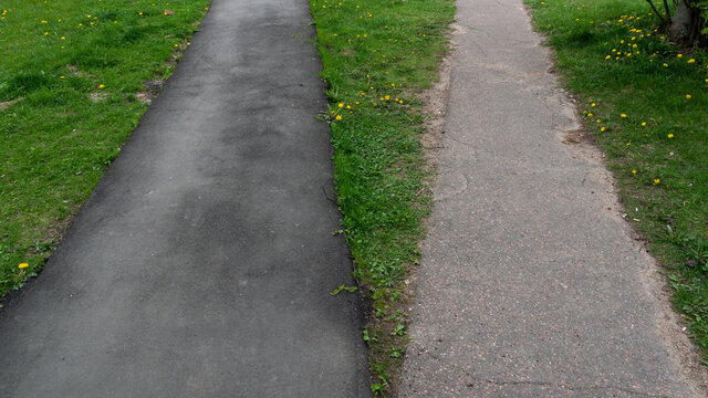 Two sidewalks from asphalt on green grass.