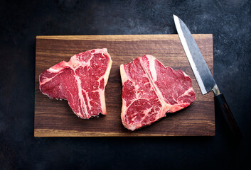 Two raw dry aged wagyu porterhouse beef steaks offered as top view on modern design wooden board...
